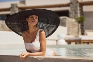 a woman in a hat sitting in the water at Hotel Milos Sea Resort in Adamantas