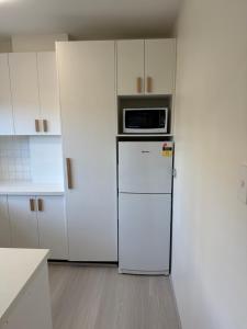 a white kitchen with a microwave on top of a refrigerator at Coogee Treehouse in Sydney +23 photos
