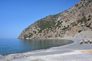 a beach with chairs and umbrellas next to the water at Calypso in Agia Roumeli