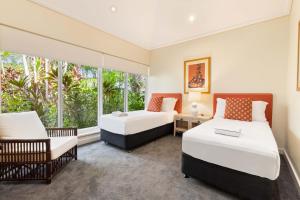 two beds and a chair in a room with windows at Mirage Resort Villa 112 with access to Sheraton Facilities in Port Douglas +3 photos