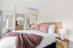 ein Schlafzimmer mit einem großen weißen Bett mit rosa Kissen in der Unterkunft Lakeside Luxe Retreat - Pool View BBQ Spa Bath in Cairns North