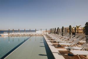 a swimming pool with lounge chairs and the ocean at DoubleTree by Hilton Malta in St Paul's Bay