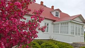 a white house with a red roof and pink flowers at BALTĀ māja in Aglona