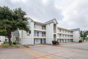 un grand bâtiment blanc avec des fenêtres bleues dans un parking dans l'établissement Motel 6-Grand Prairie, TX - Near Six Flags Drive, à Grand Prairie