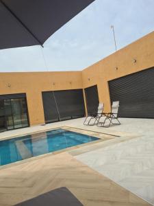 a swimming pool with two chairs and a building at Villa avec piscine privée in Oulad Akkou