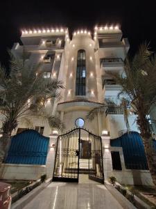 a large white building with a gate and palm trees at العجمي 300 in 6th Of October