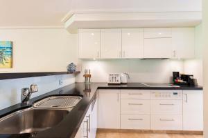 cocina con armarios blancos y fregadero de acero inoxidable en Mirage Resort Villa 142 with access to Sheraton Facilities, en Port Douglas