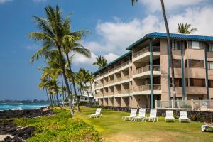 un hotel sulla spiaggia con sedie e palme di CASTLE at Kona Reef a Kailua-Kona