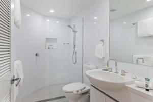 a white bathroom with a shower and a toilet and a sink at Mirage Resort Villa 456 with access to Sheraton Facilities in Port Douglas +2 photos