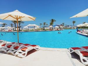 a swimming pool with chairs and umbrellas at Marselia beach 4 bianca 14 in Sīdī ‘Abd ar Raḩmān