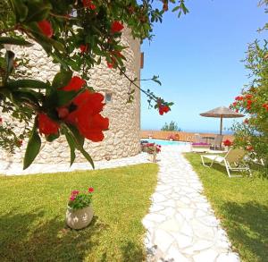 a pathway leading to a building with a pool and flowers at Anemomilos Villa in Asprogerakata