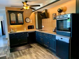 a large kitchen with blue cabinets and a ceiling fan at Le 007 Refuge -Rurale gîte élégant piscine privée in Queyssac