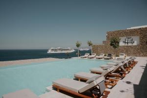 a swimming pool with lounge chairs and a cruise ship at Tagoo Hills in Mikonos