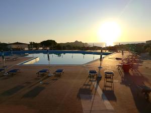 a large swimming pool with chairs and the sun setting at Appartamento Calarossa Sardegna CasaRosa in Isola Rossa