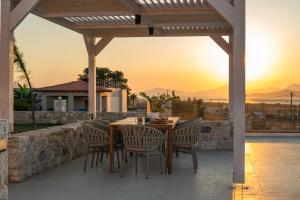 einen Holztisch und Stühle auf einer Terrasse mit Blick auf den Sonnenuntergang in der Unterkunft Villa Jaubelli Bliss in Platánion
