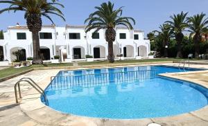 a pool in front of a white house with palm trees at Apartamento Ciutadella con piscina en Son Xoriguer - Menorca in Son Xoriguer