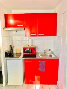 een rode keuken met een magnetron en een wastafel bij La Cabane de Riva Bella in Ouistreham