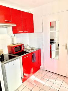 een rode keuken met een wastafel en een magnetron bij La Cabane de Riva Bella in Ouistreham