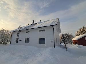 a white house in the snow next to a barn at Rooms in a big wooden home, homestay in Muonio