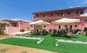 ein rosafarbenes Gebäude mit einem Hof mit Tischen und Sonnenschirmen in der Unterkunft Venias Rooms in Skala Eresou