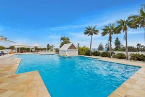 a large blue swimming pool with palm trees at The Entrance Waterfront Apartment 505 in The Entrance