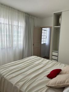 a bedroom with a white bed with a red pillow at Nossa casa, nosso lar in Belo Horizonte