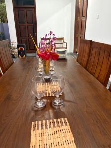 a wooden table with a vase of flowers and glasses at Hikka Garden Villa in Hikkaduwa