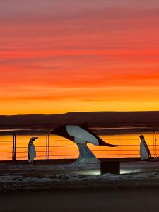 a painting of three penguins standing in front of the ocean at Puesta del Sol Apart in Río Gallegos