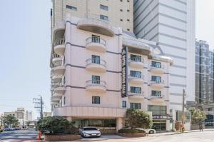 a tall white building with a car parked in front of it at Morning Calm Jeju in Jeju