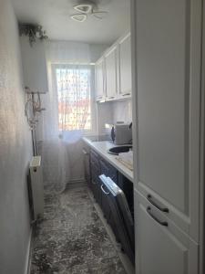 una pequeña cocina con armarios blancos y una ventana en Apartament Cristi, en Bistriţa
