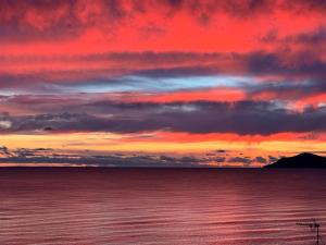 a sunset over a body of water with a mountain at Absolute Beachfront Holiday Home With Private Beach Access To Swim Beach Spectacular Sunsets in Paraparaumu