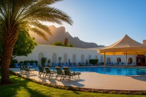 a resort with a pool and chairs and a palm tree at Falaj Daris Hotel in Nizwa