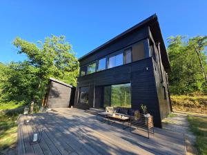 a black house on a wooden deck with chairs at Blackberry Cabin lakeside escape in Tubravić