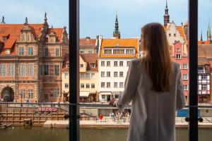 a woman looking out of a window at buildings at Flatbook - City Center SPA Apartments Deo Plaza Studio II in Gdańsk