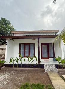 a white house with red windows and plants in front at Cena Homestay in Mantaak