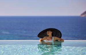 a woman in a hat sitting in a swimming pool at Hotel Milos Sea Resort in Adamantas
