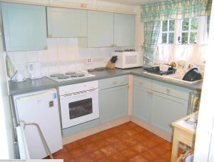 a kitchen with blue cabinets and white appliances at Traditional 2 Bedroom Thatched Cottage in East Budleigh +1 photo