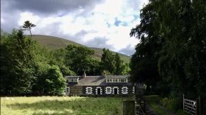 una casa en un campo con una colina en el fondo en Wood Cottage, en Peebles