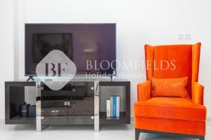 Una silla naranja y una mesa de cristal con un televisor. en Bloomfields 1Br Golfside Getaway Damac Hills, en Dubai Marina