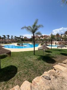 a resort with a large swimming pool with a palm tree at Almerimar Amplio Apartamento de 3 Habitaciones con Piscina, pista de padel, futbol y Garaje Cubierto para 2 Coches en Altas Entinas in Almerimar