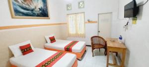 a room with two beds and a desk and a television at Wisma Narita in Lampung