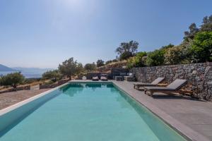 a swimming pool with chairs and a stone wall at Villa Melisea in Sfendoúrion