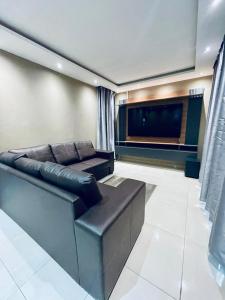 a living room with a leather couch and a flat screen tv at Que Self Catering Apartments in Gaborone
