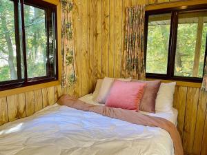 a bed in a wooden room with two windows at Upper Boathouse on Balsam Lake #1 in Kawartha Lakes