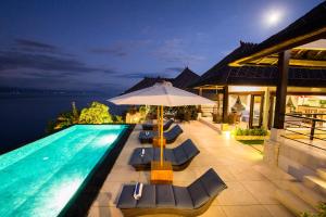 a swimming pool with lounge chairs and an umbrella at The Point Resort Lembongan in Nusa Lembongan