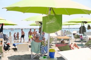 eine Gruppe von Menschen, die unter einem Sonnenschirm am Strand sitzen in der Unterkunft Family Hotel Mediterraneo - Azzurro Club in Cesenatico