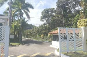 an empty street with a white gate and palm trees at casa com piscina da edi fontes in Guarujá