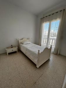 a white bedroom with a bed and a window at Appartement spacieux - Dar Chaabane plage in Nabeul
