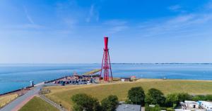 a red tower on a hill next to the water at KÜSTE33/20 – Exklusive Ferienwohnung mit Sauna & nah am Strand! in Butjadingen OT Tossens
