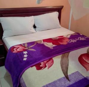 a bed with a purple and white comforter with flowers on it at Bali Hotel Palace in Yaoundé